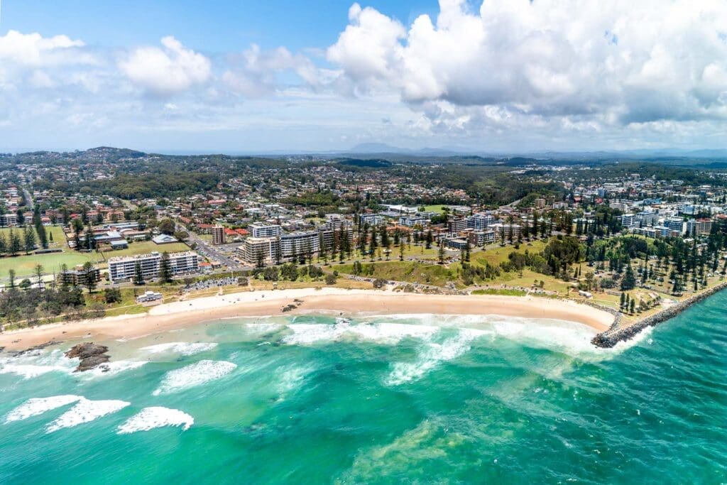 Aerial view of Port Macquarie coastline with beach, surf and town buildings.
